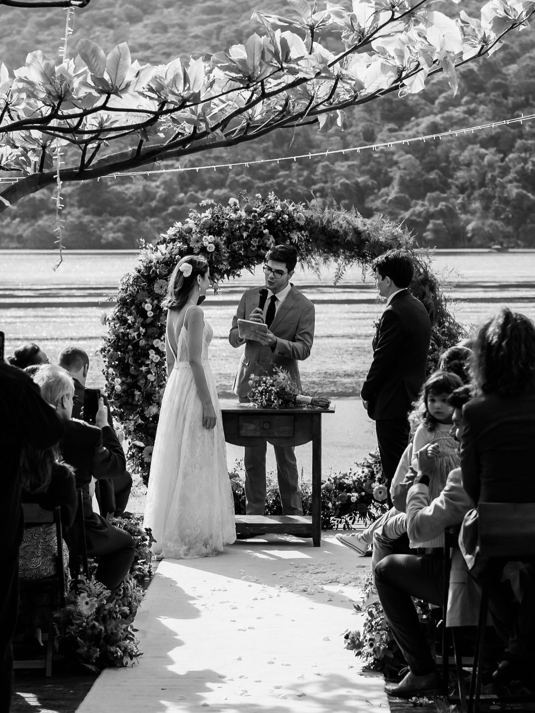 Murilo Mestriner celebrando um casamento ao ar livre sob um arco de flores, em preto e branco